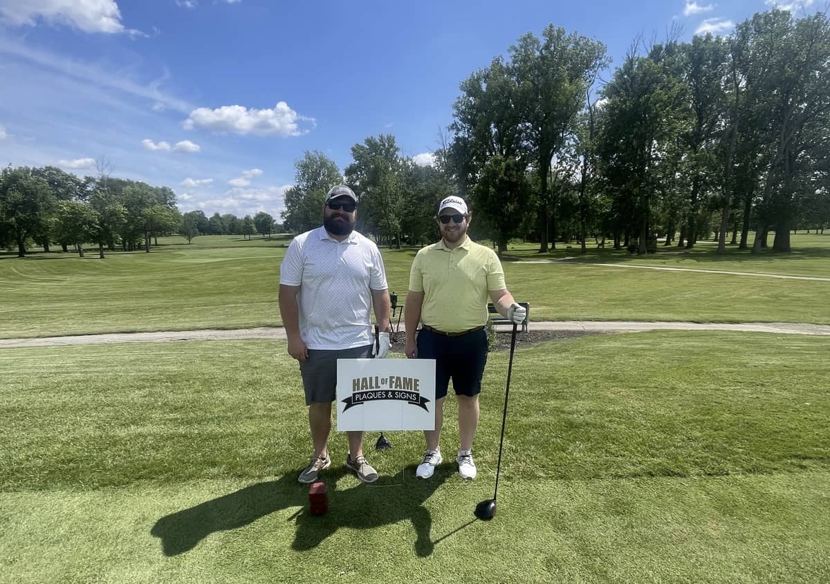 2 men in front of a sign for Hall of Fame Plaques for a Golf Outing