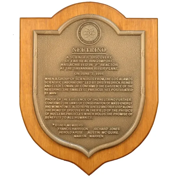 Shield-shaped bronze historical discovery plaque mounted on a solid wood backing featuring a scientific atom logo.