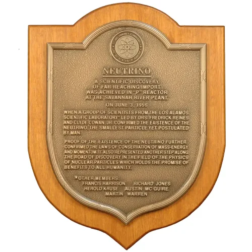 Shield-shaped bronze historical discovery plaque mounted on a solid wood backing featuring a scientific atom logo.
